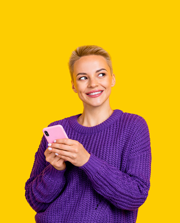 A lady with short blonde hair and a purple sweater holding a phone and looking up against a yellow background